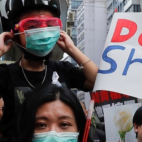 A woman and a child wearing protective gear joins tens of thousands of protesters marching through the streets in protest of an extradition bill.