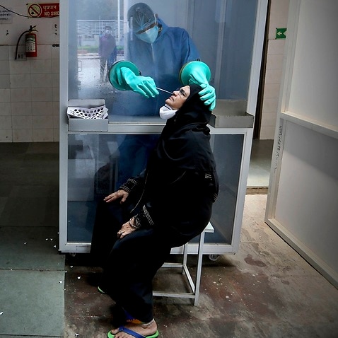 A health worker takes a nasal swab of a woman for COVID-19 test at a hospital in New Delhi, India.