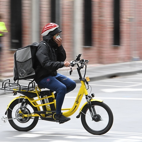 A delivery driver on a bike is seen adjusting their mask in Melbourne, Wednesday, March, 25, 2020.