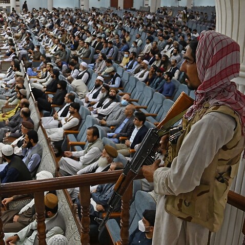 A Taliban fighter stands guard as acting higher education minister addresses a gathering on the Taliban's higher-education policies Aug. 29