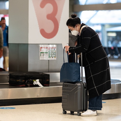 Passengers wearing face masks collect their baggage.