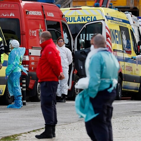 ambulance personnel stand waiting as more than a dozen ambulances queue waiting to hand over their COVID-19 patients to medics at the Santa Maria hospital in Lisbon