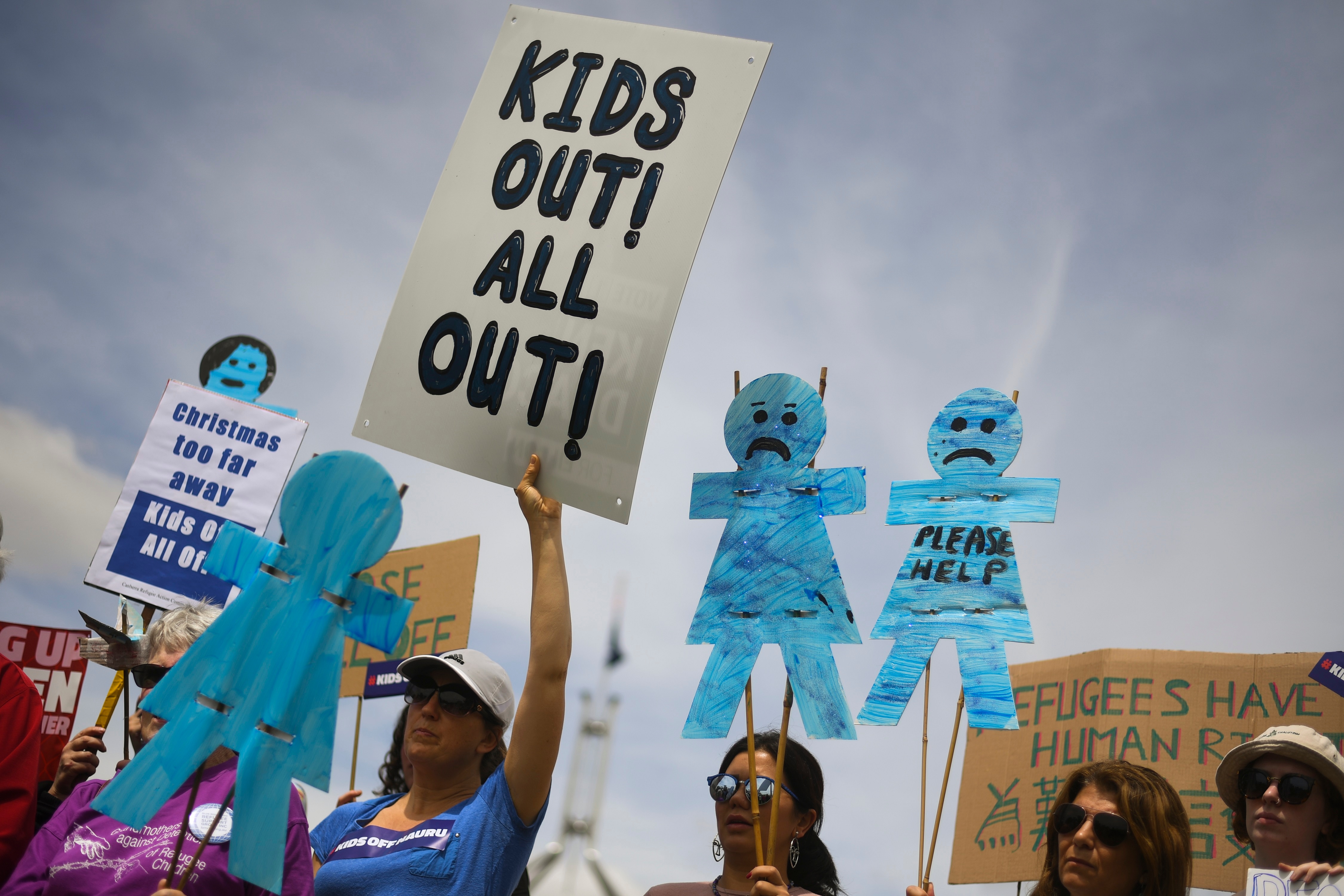 Protesters hold up signs during a rally demanding the resettlement of kids held on Nauru outside Parliament House in Canberra, Tuesday, November 27, 2018.