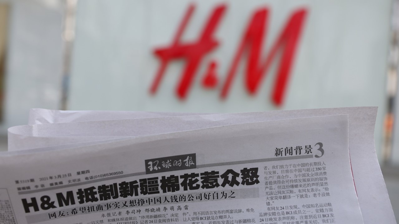 A newspaper with a report about H&M is seen in front of a H&M logo 