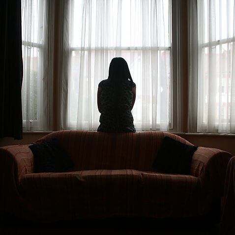 A young Asian woman suffering from domestic violence stands alone in the bay window of her home. (Photo by In Pictures Ltd./Corbis via Getty Images)