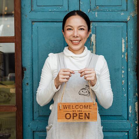 Female cafe owner showing WELCOME WE ARE OPEN inscription
