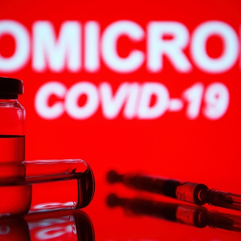 In this photo illustration, a medical syringe and two vials are seen in front of the text Omicron COVID-19 in the background. (Photo by Pavlo Gonchar / SOPA Images/Sipa USA)