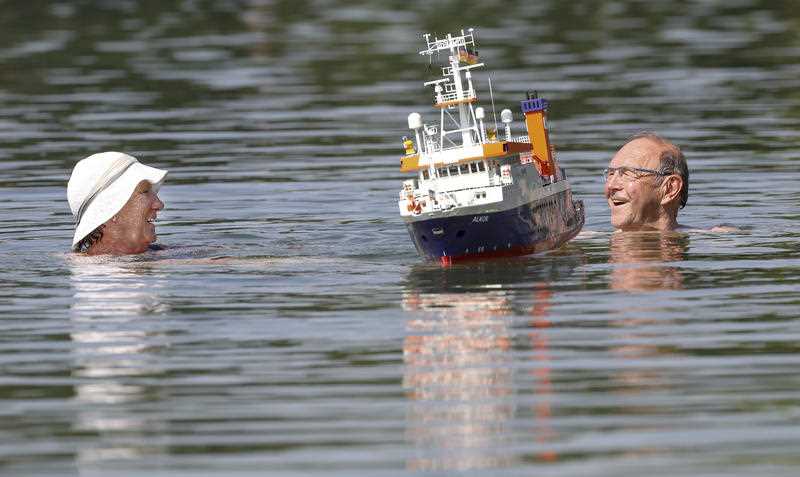 A couple swims beside a model boat in a lake in Ertingen, Germany, on Wednesday.