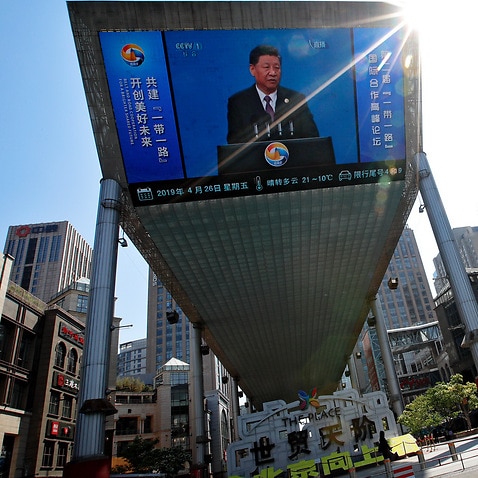 People pass by a TV screen broadcasting live of President Xi Jinping's opening speech.