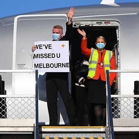 Flight crew wave to media holding a sign in the doorwell of Jetstar flight JQ505 which arrived from Sydney at Tullamarine Airport in Melbourne.