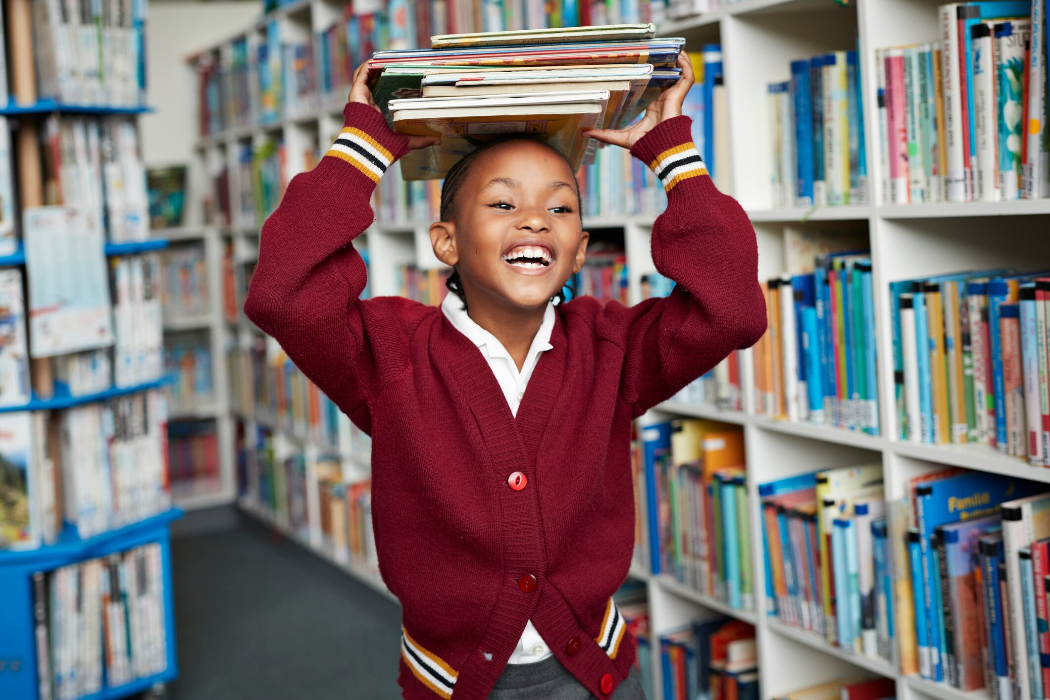 Cute schoolgirl smiling & balancing stack of books on the head at library
