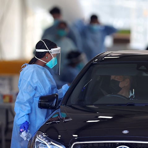 Health staff are seen as members of the public queue in their cars at a drive-through COVID-19 testing site in Melbourne.
