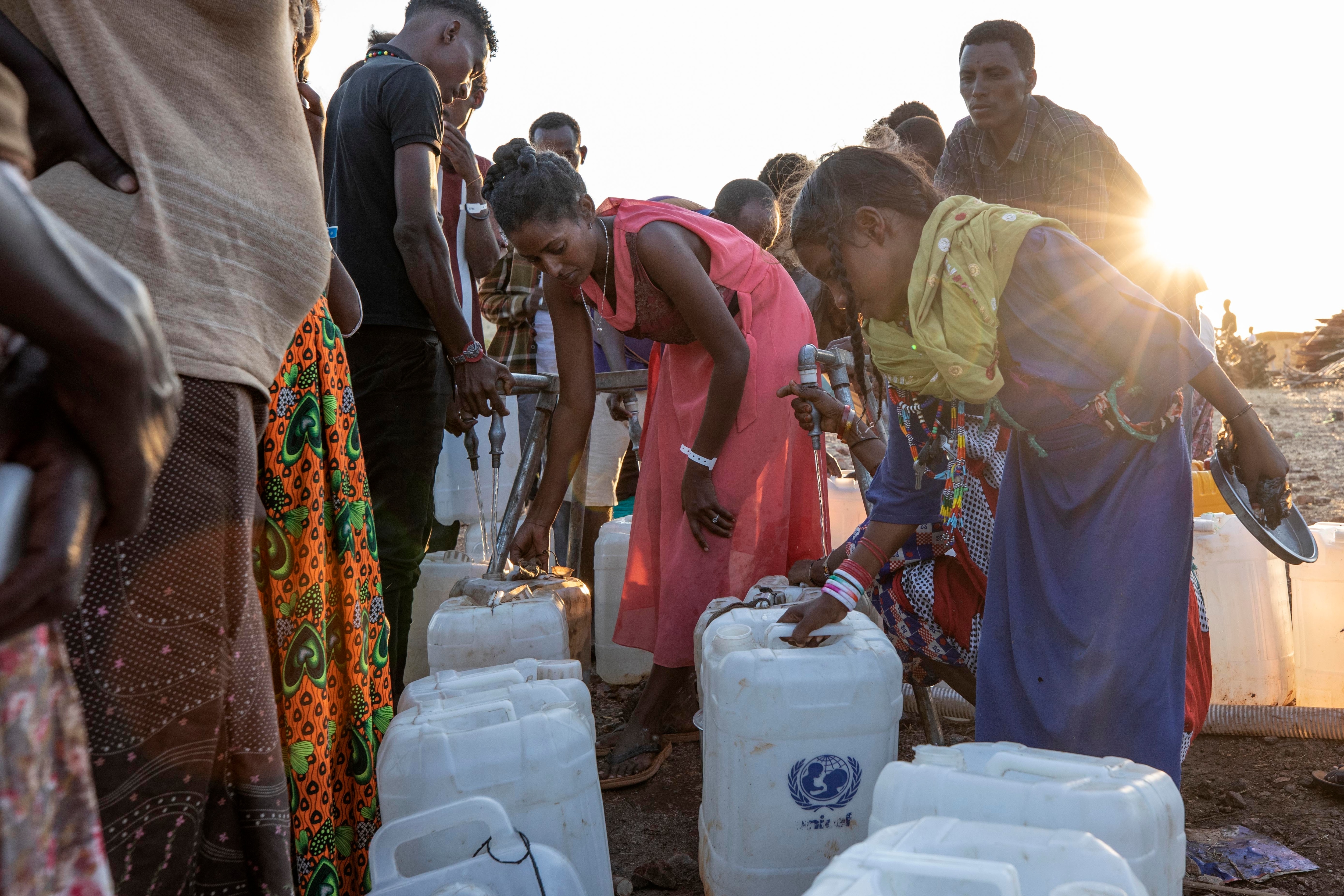 Women who fled a conflict in Ethiopia's Tigray region, and a Sudanese girl from a tribe living near by, pour water into gallons at a eastern Sudan refugee camp.