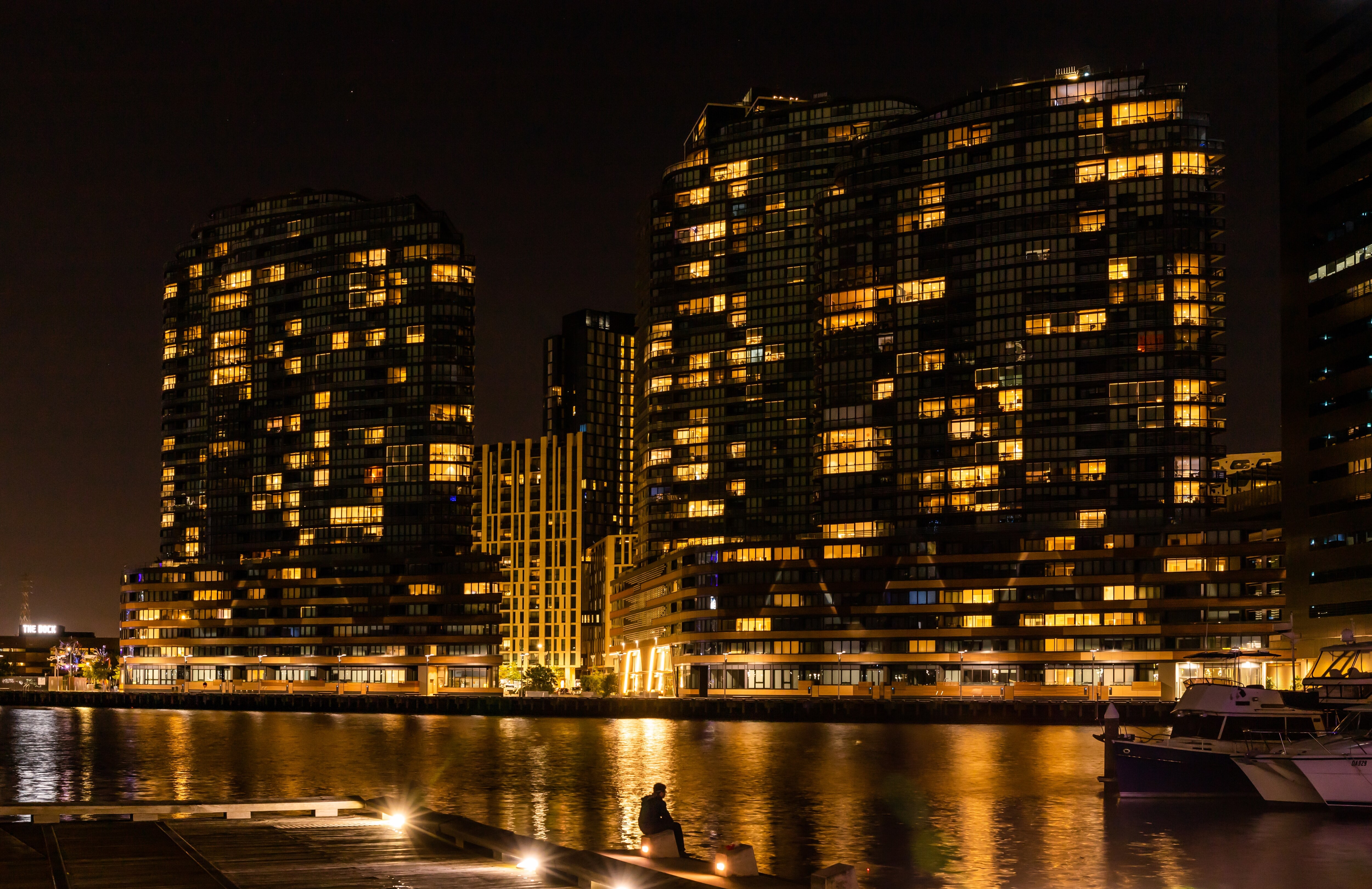 A man sitting on pier beside illuminated high buildings at night
