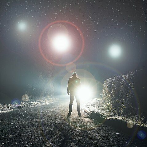 Glowing orbs, floating above a misty road at night with a silhouetted figure