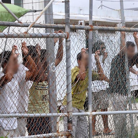 Asylum seekers staring at media from behind a fence at the Manus Island detention centre