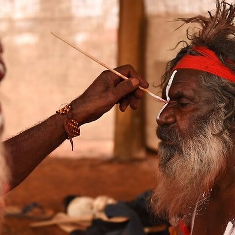 An Aboriginal elder paints a fellow elder before dancing at a cultural event near Uluru