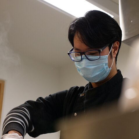 A young man wearing a mask working in a kitchen