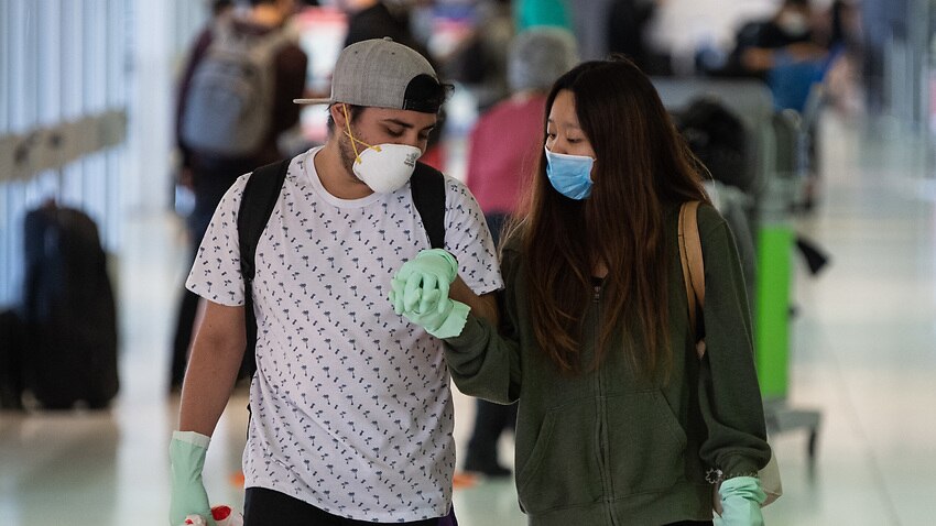 A file photo of a couple holding hands whilst wearing protective gloves and masks in the departures area at the Sydney International Airport.