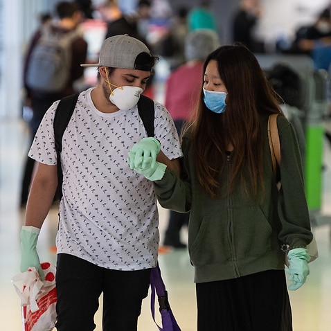 A file photo of a couple holding hands whilst wearing protective gloves and masks in the departures area at the Sydney International Airport.