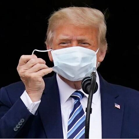 President Donald Trump removes his face mask to speak from the Blue Room Balcony of the White House to a crowd of supporters.