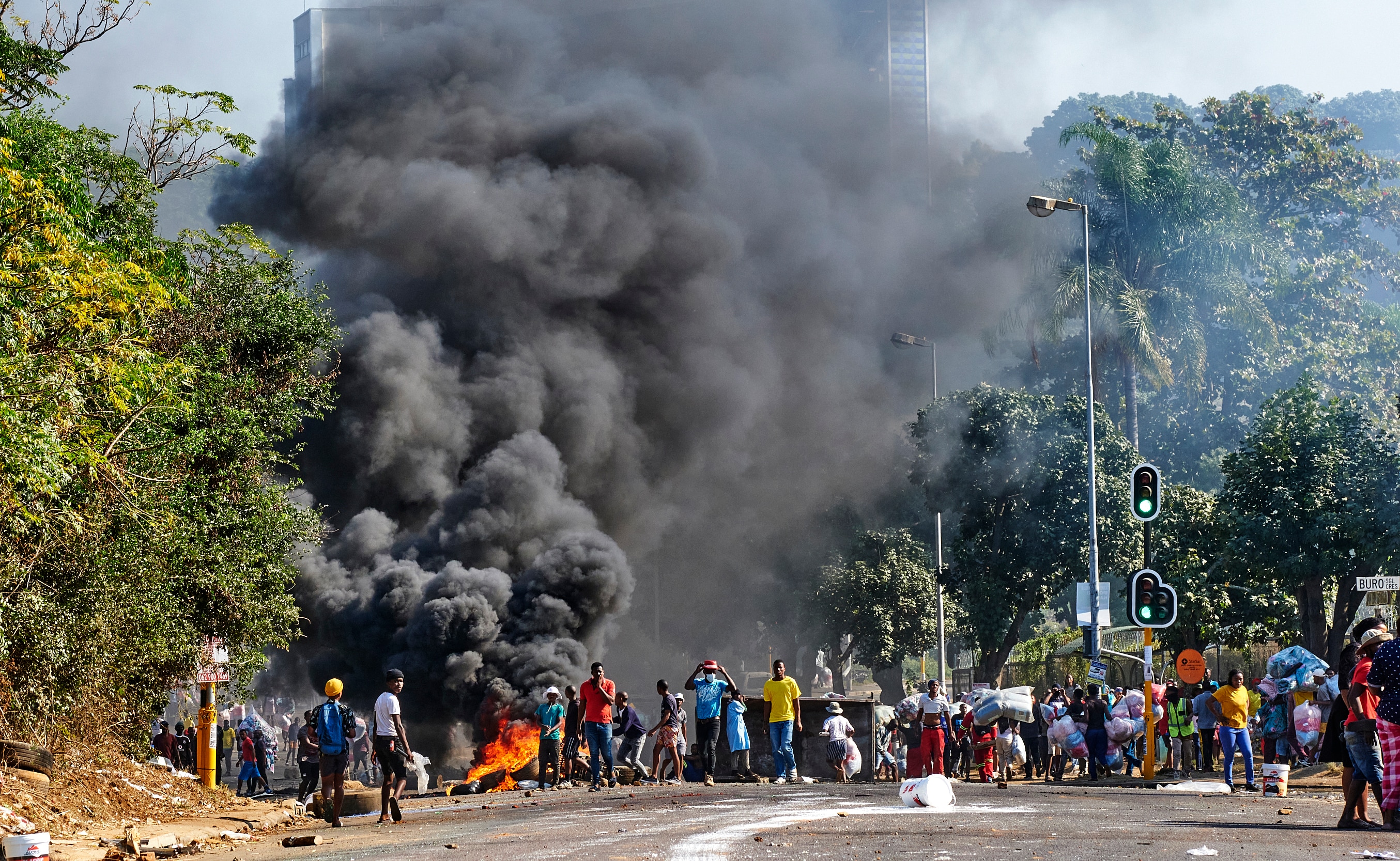 Looters outside a shopping centre alongside a burning barricade in Durban, South Africa, Monday July 12, 2021