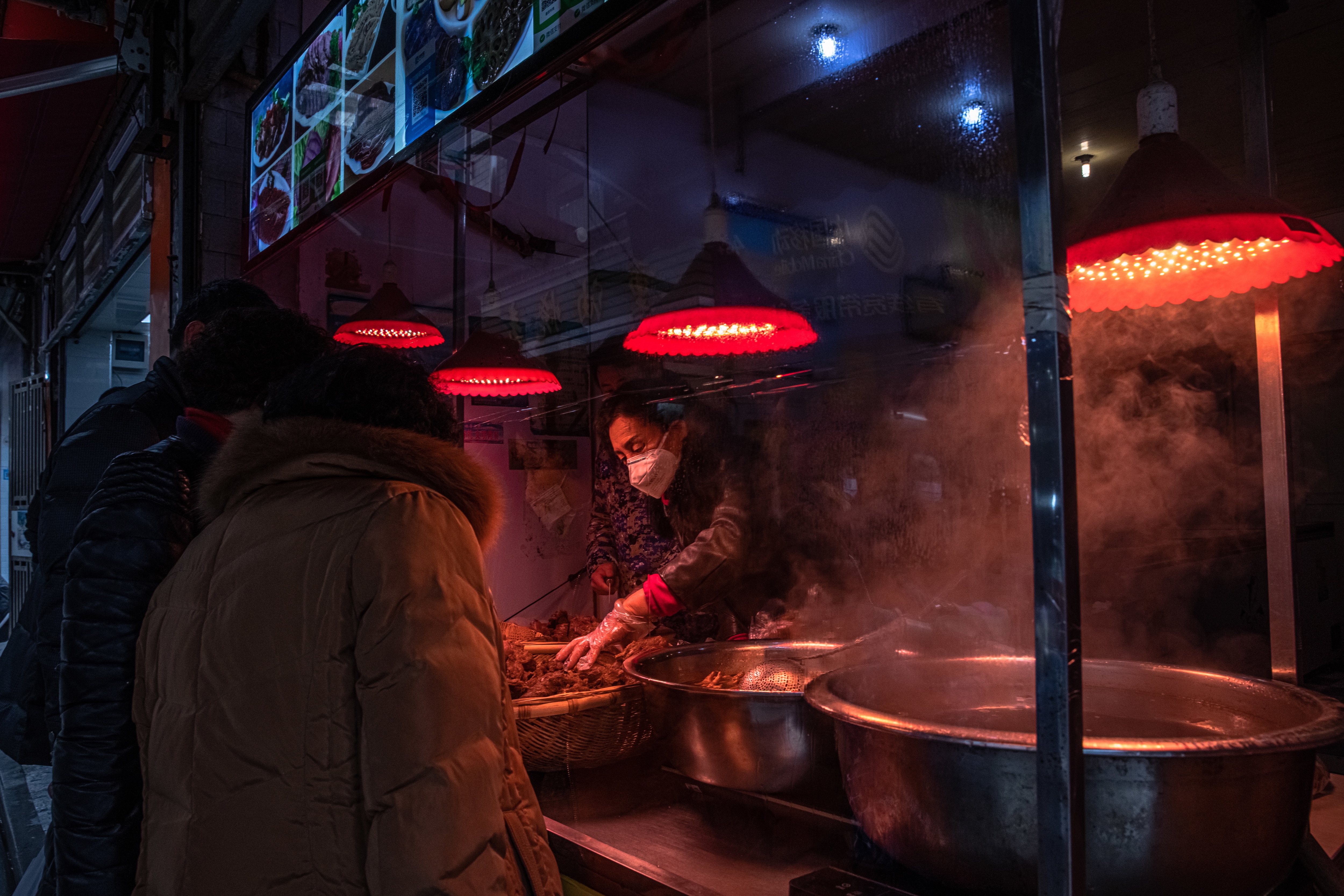 A woman wearing a protective face mask sells food to customers at a small restaurant in a residential area of Wuhan, China, on 22 January, 2021. 