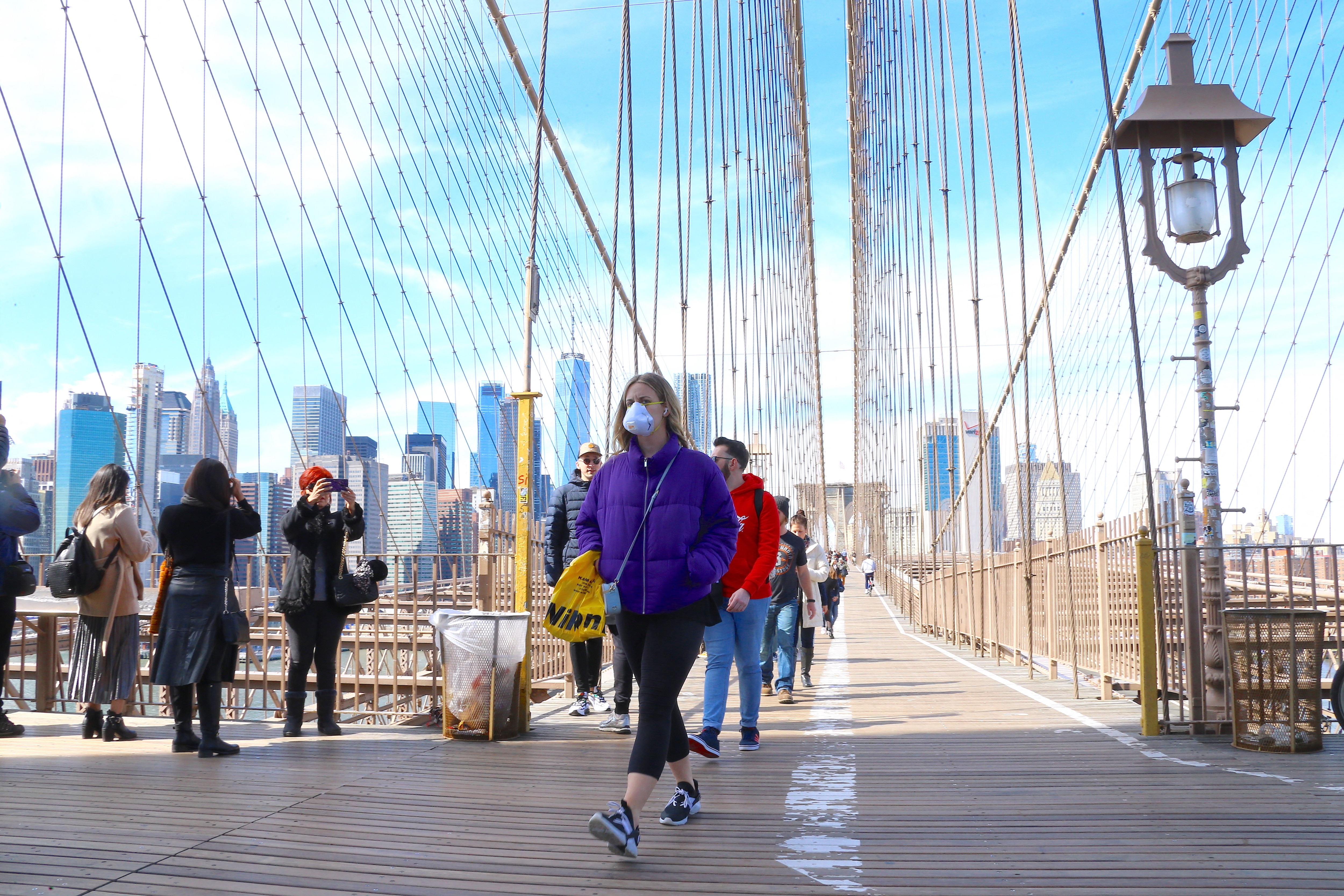 Tourists with face mask walk the Brooklyn Bridge on Saturday afternoon in New York.