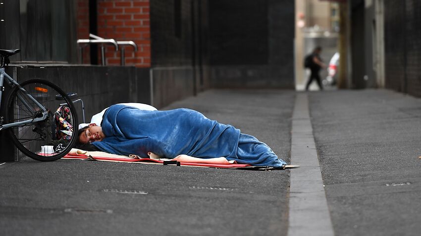 A homeless man sleeps in a laneway.