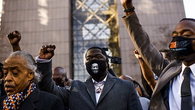 Brandon Williams trägt eine Maske und einen Anhänger mit dem Bild seines Onkels George Floyd und hebt die Faust im Gerichtsgebäude in Minneapolis, Minnesota.
