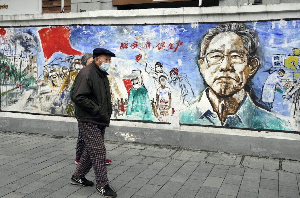 Residents wearing masks walk past a mural on the eve of the anniversary of the first COVID-19 lockdown in Wuhan, 22 Jan 2021.