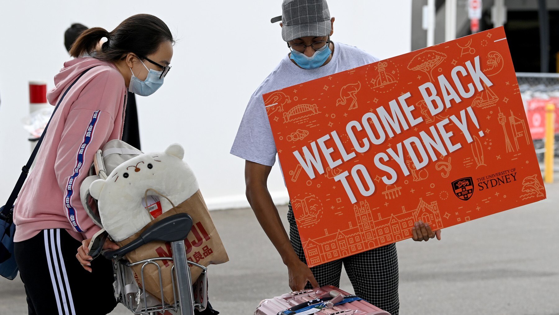 University representatives hold signs as international students arrive at Sydney Airport in Sydney. AAP