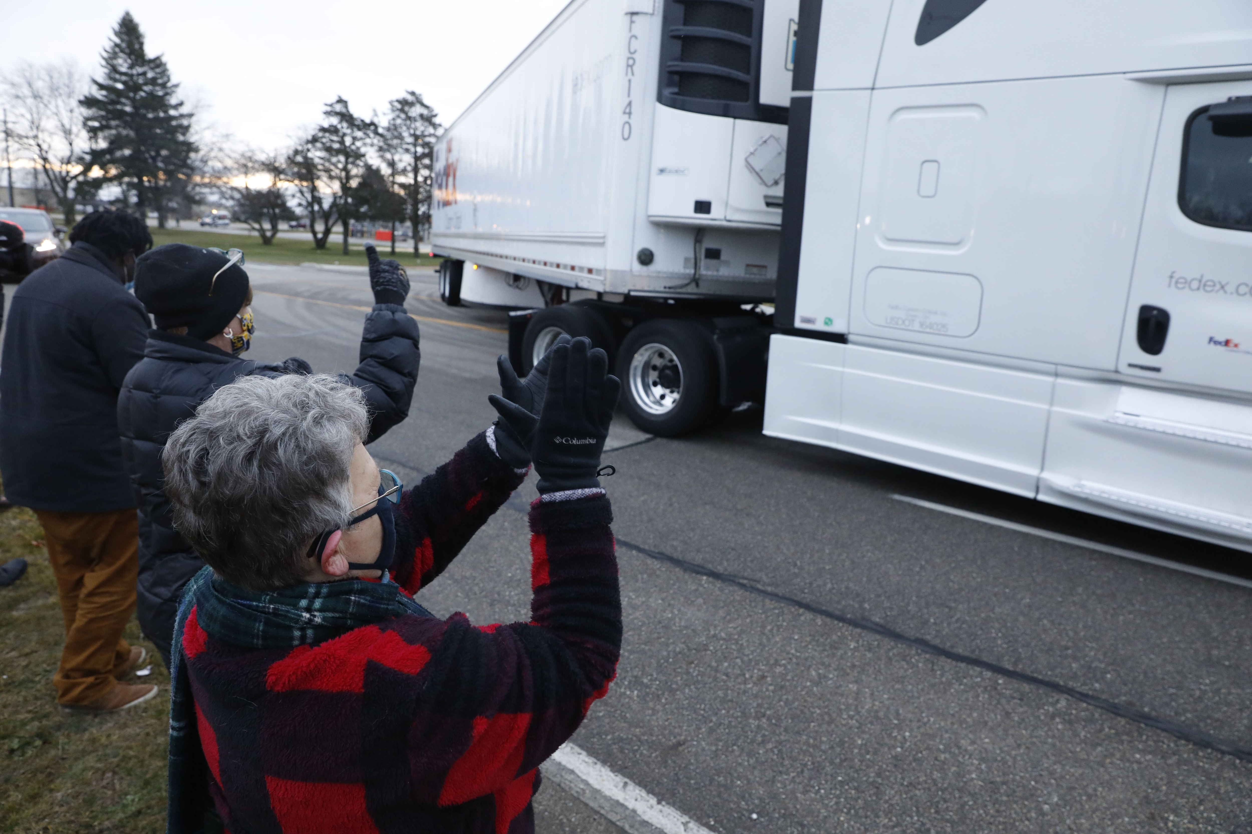 People cheer as trucks carrying the first shipment of the COVID-19 vaccine leaves Pfizer's Global Supply facility in Kalamazoo, Michigan on 13 December, 2020.