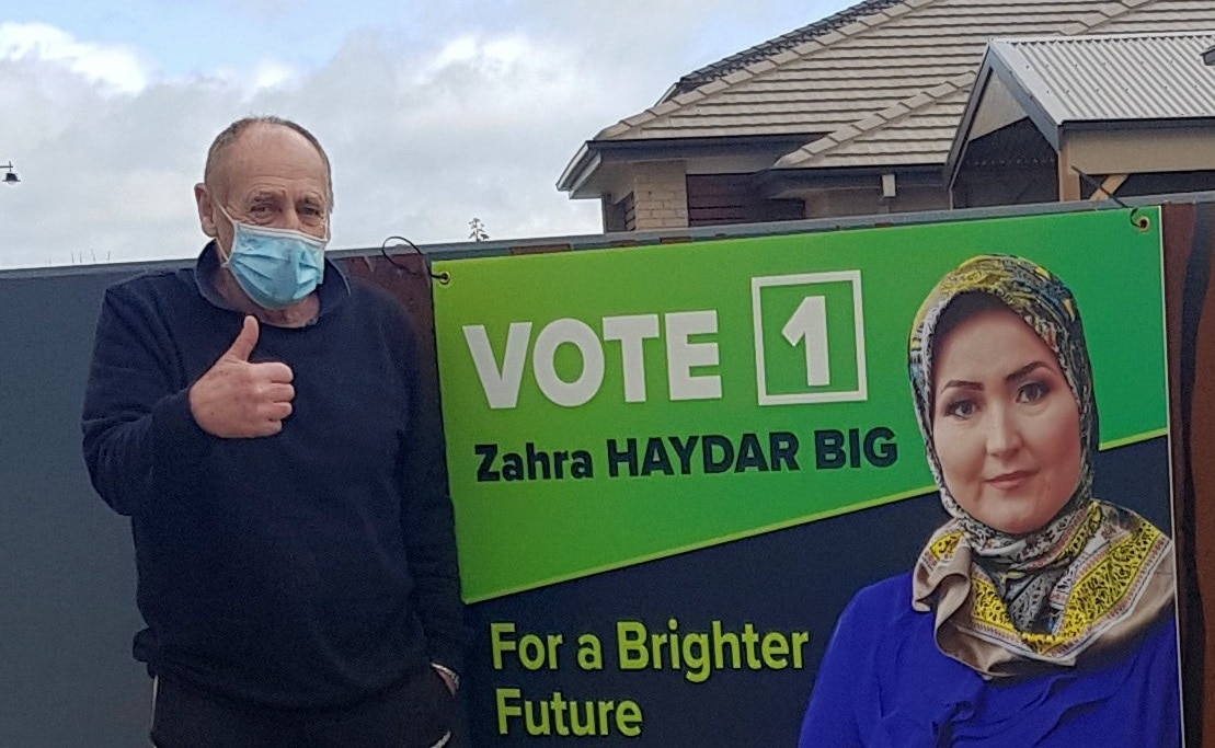 Zahra Haydarbig’s campaign manager Leo Houlihan posing next to her poster.