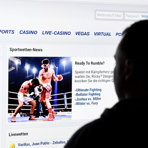 A man stands in front of a screen with a page of a sports betting provider (bet-at-home).
