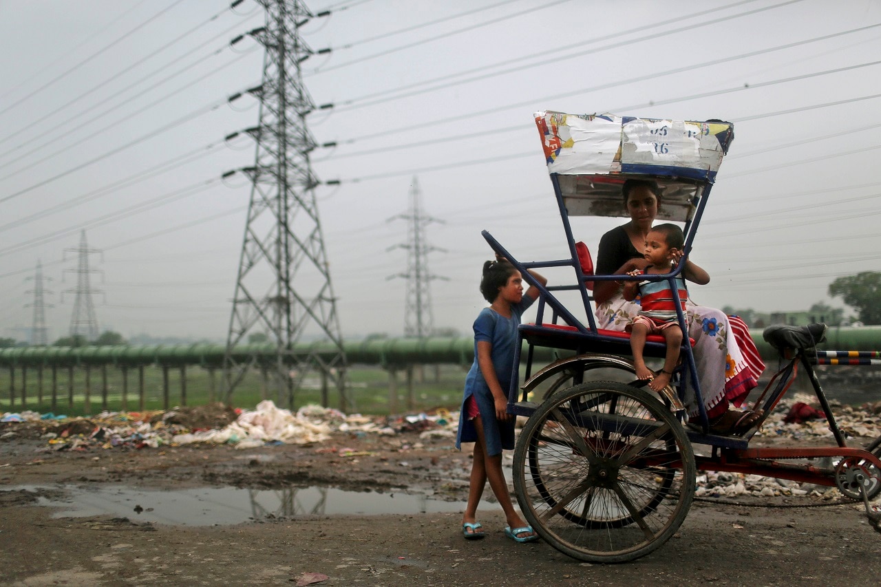 An Indian woman and her children sit on a bicycle rickshaw near high tension electricity towers on a roadside in New Delhi, India,