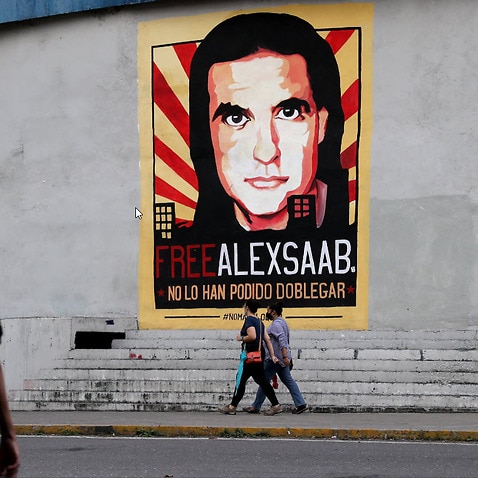 People pass in front of a cartel to show support to Colombian-Venezuelan businessman Alex Saab in Caracas, Venezuela, 17 October 2021.