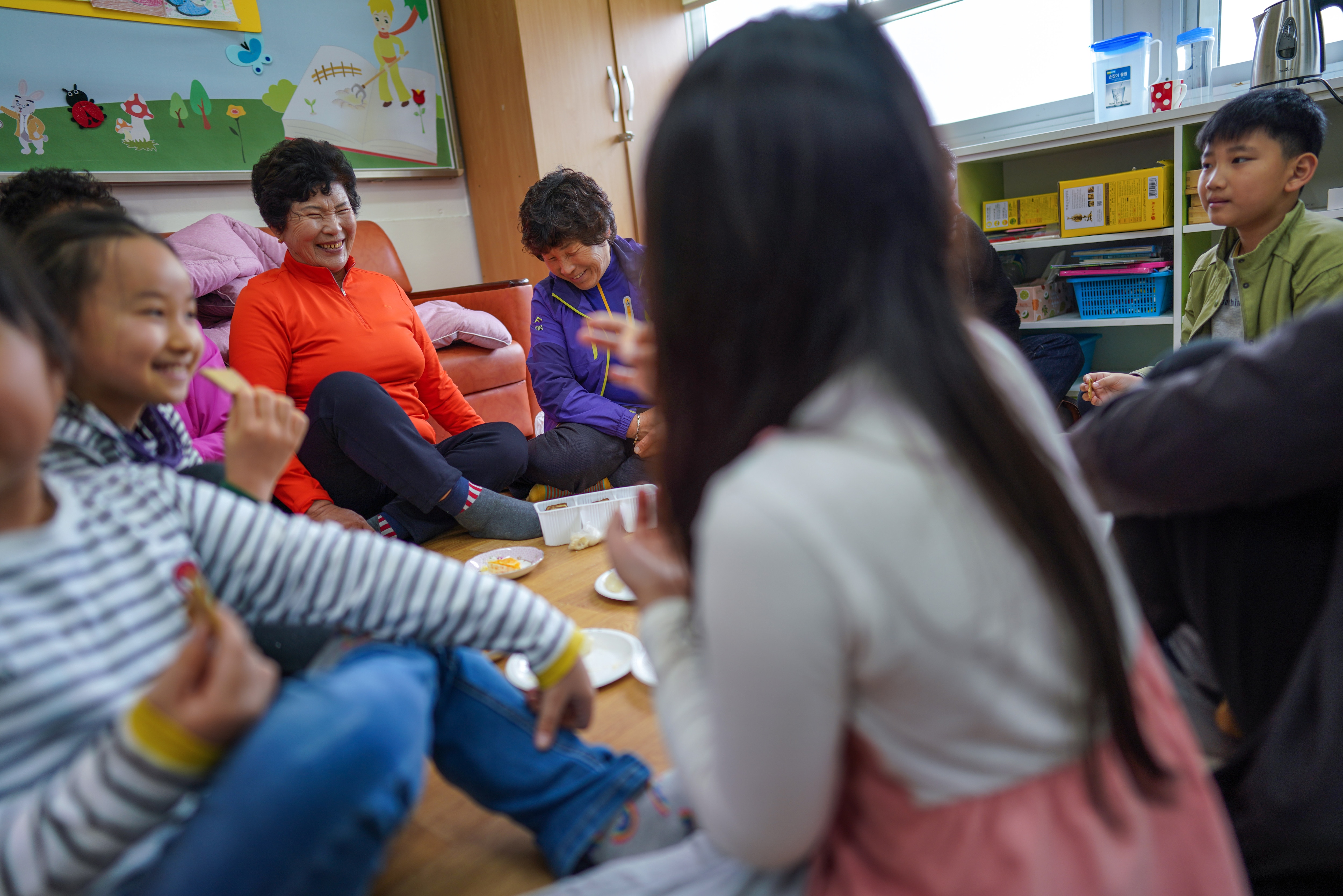 Hwang Wol-geum, 70, left, and Kim Mae-ye, 64, share snacks with students. Hwang Wol-geum, 70, left, and Kim Mae-ye, 64, share snacks with students at Daegu Elementary, in Gangjin County, South Korea.
