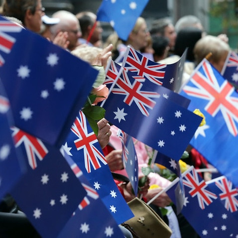 People wave flags as an ANZAC Day parade marches by in Sydney, Australia, Saturday, April 25, 2015.