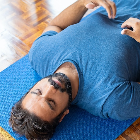 Man lying on yoga mat with eyes closed, meditating