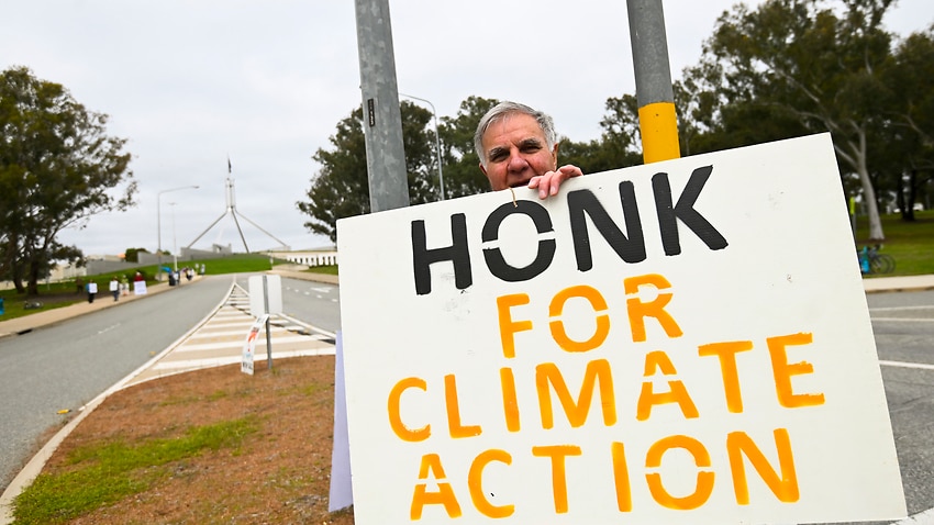 People hold banners as they participate in a climate protest outside Parliament in Canberra.