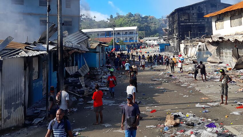 People gather as smoke rises from a burnt out building in Honiara's Chinatown on 26 November, 2021.