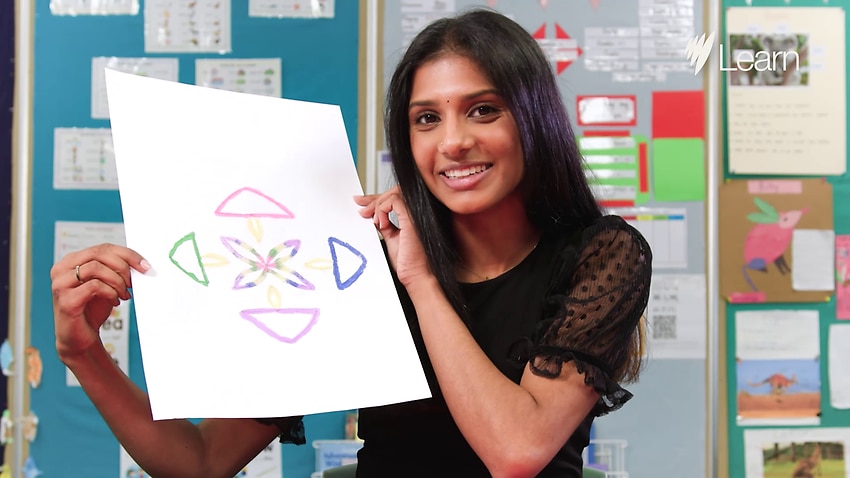 An South Asian female teacher in a classroom holding artwork