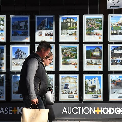 A couple walks past a real estate agent's window advertising houses for sale and auction in Melbourne.