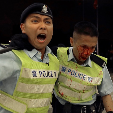 A Hong Kong police officer with blood flowing down his face is assisted by his colleague (AAP)