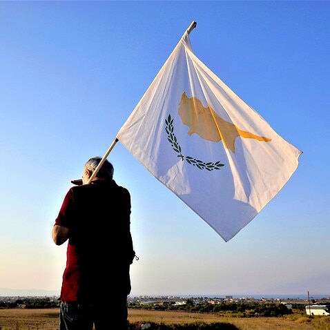 A man with a Cyprus flag stands in front of the Varosha or Famagusta, abandoned city. 