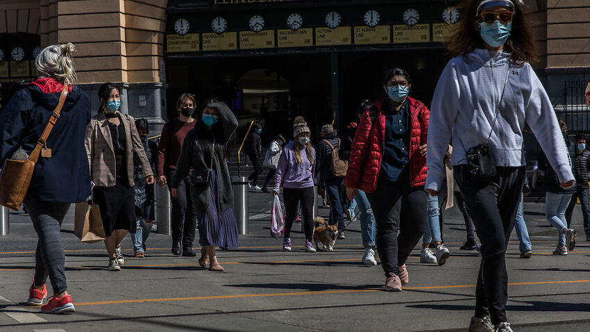 Pedestrians cross a street outside Flinders Street Station on 24 October, 2021 in Melbourne.
