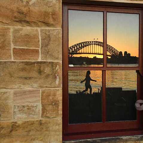 Sydney Harbour Bridge kıyısında yürüyen bir kadının pencereye yansıyan görüntüsü 