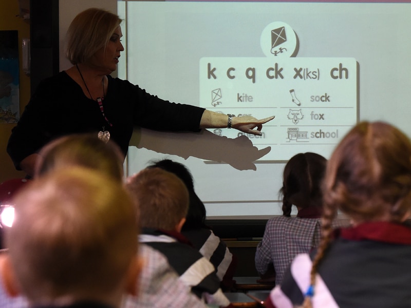 A teacher points at a board during a lesson