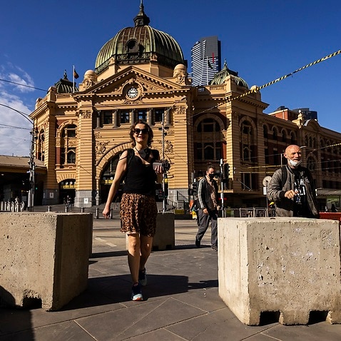 People are seen walking across Flinders Street in Melbourne.
